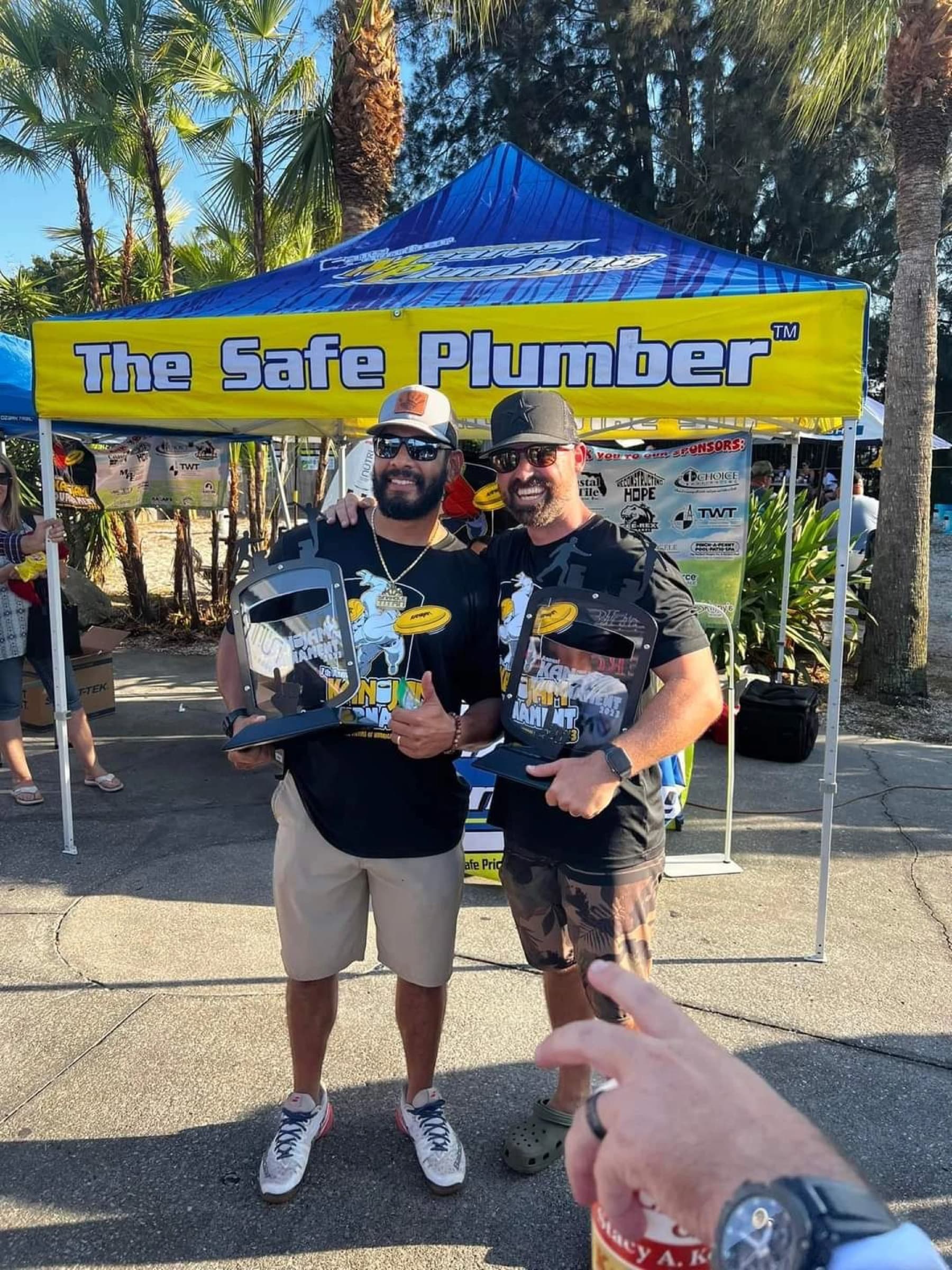 Past Can Jam champions hoisting their trophies under the Safe Plumber tent